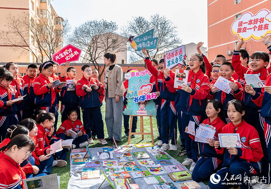 4月17日，呼和浩特市玉泉区南茶坊小学学生在“图书漂流”集市上向伙伴推荐摊位上准备交换的图书。丁根厚摄